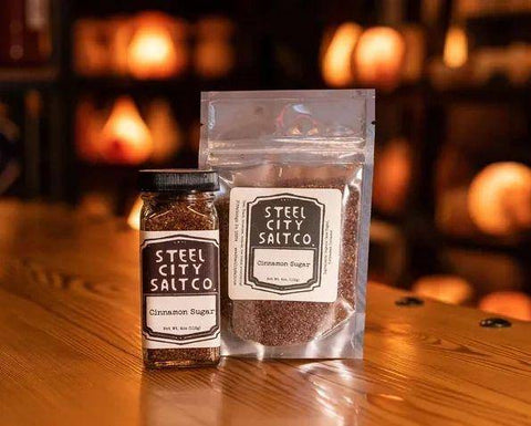 Cinnamon Sugar by Steel City Salt Company displayed in a jar and resealable pouch on a wooden table with warm ambient lighting. Available at Huckle Bee Farms LLC.