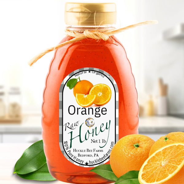 Orange-infused raw honey in a 1lb jar with a natural twine bow, set against a kitchen backdrop with fresh oranges. A citrus twist on pure honey.