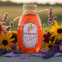 Jar of Huckle Bee Farms raw wildflower honey surrounded by seasonal wildflowers — rich golden color and handcrafted jar