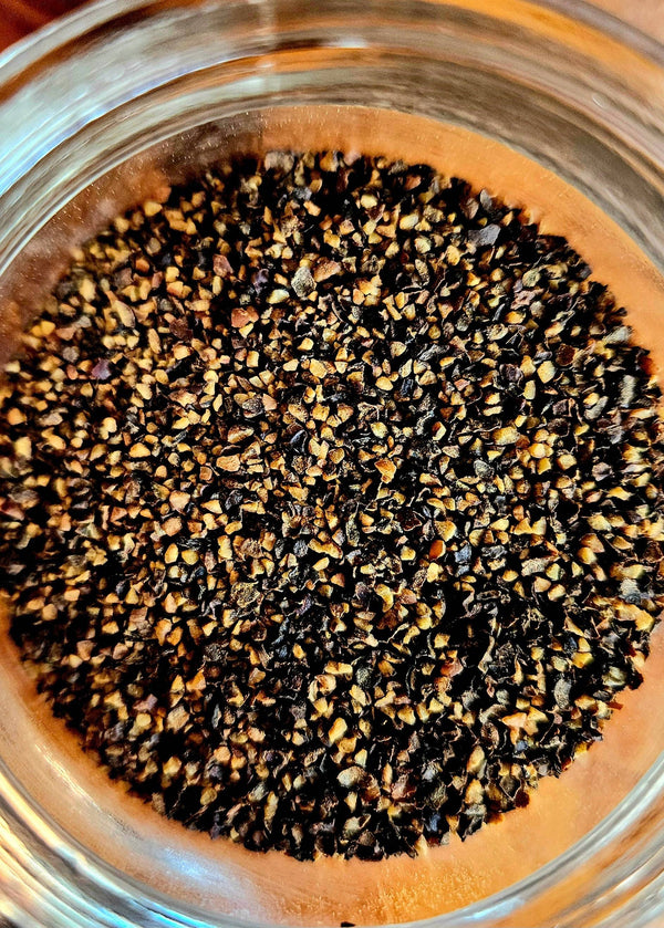 Close-up of coarse Applewood Smoked Black Pepper granules. Premium smoky seasoning ideal for enhancing grilled meats and savory dishes.