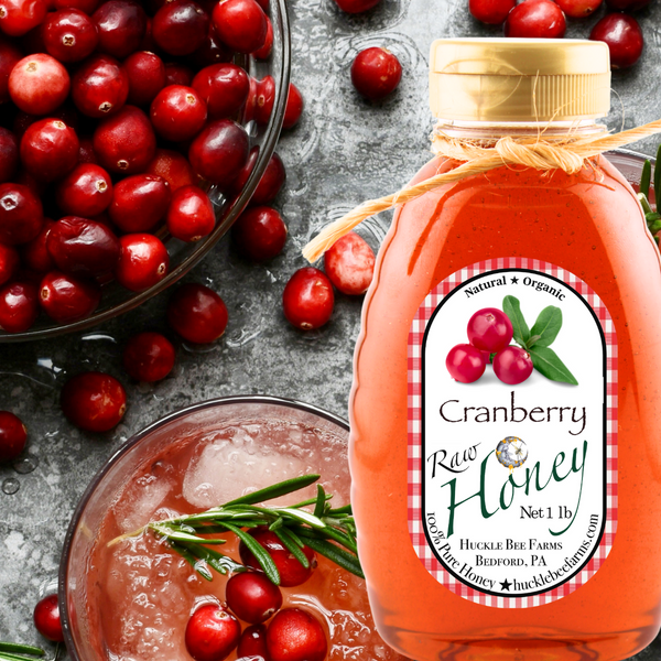 Bottle of Cranberry Raw Honey with cranberries and a cocktail on a gray surface