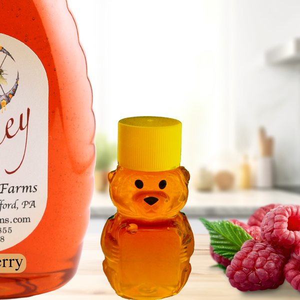 Adorable bear-shaped honey bottle beside a raspberry infused honey jar, featuring a bright yellow cap and fresh raspberries in a kitchen setting.