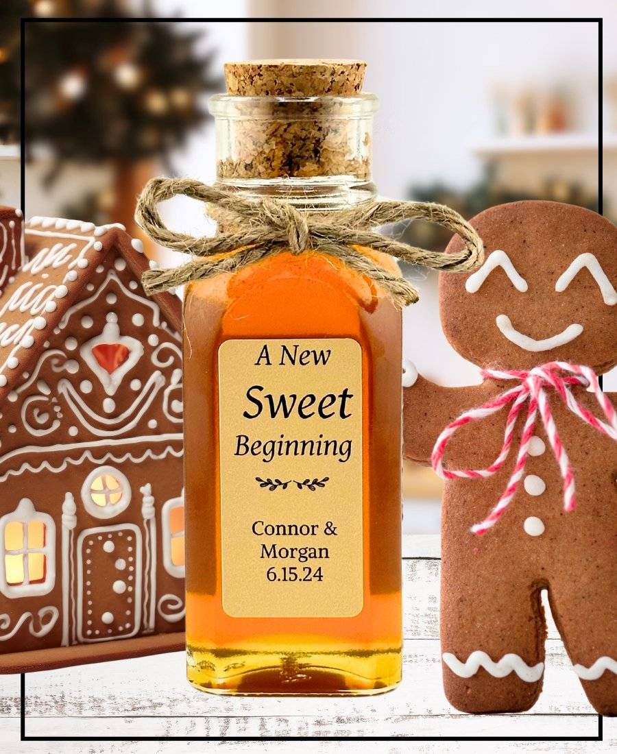 Personalized gingerbread honey bottle with a cork lid, tied with twine, labeled 'A New Sweet Beginning' with names Connor & Morgan and date 6.15.24. Surrounded by festive gingerbread cookies and a decorated gingerbread house.