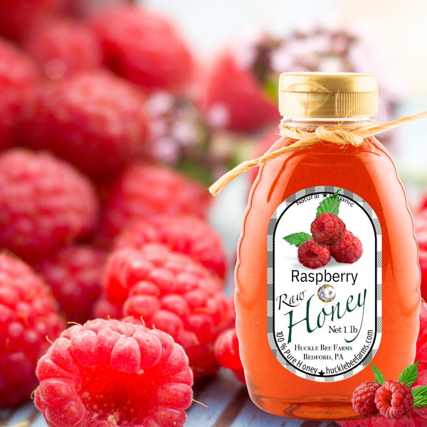 Close-up of raspberry infused honey in a decorative jar, surrounded by fresh raspberries, highlighting its fruity sweetness and natural ingredients.