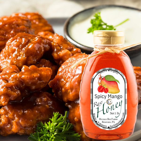 Spicy Mango Honey bottle placed in front of saucy spicy chicken wings with a side of ranch, showcasing its bold and flavorful culinary use.