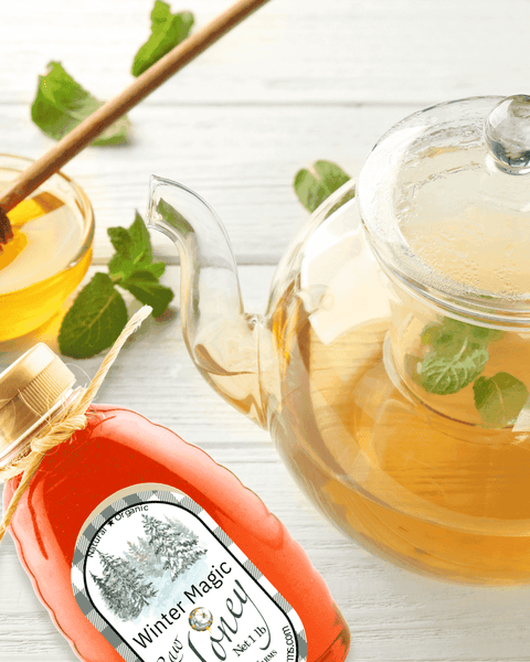 Winter Magic Honey by Huckle Bee Farms LLC displayed with a glass teapot of mint tea, a honey dipper, and fresh mint leaves. Premium fruit-infused honey for beverages and recipes.